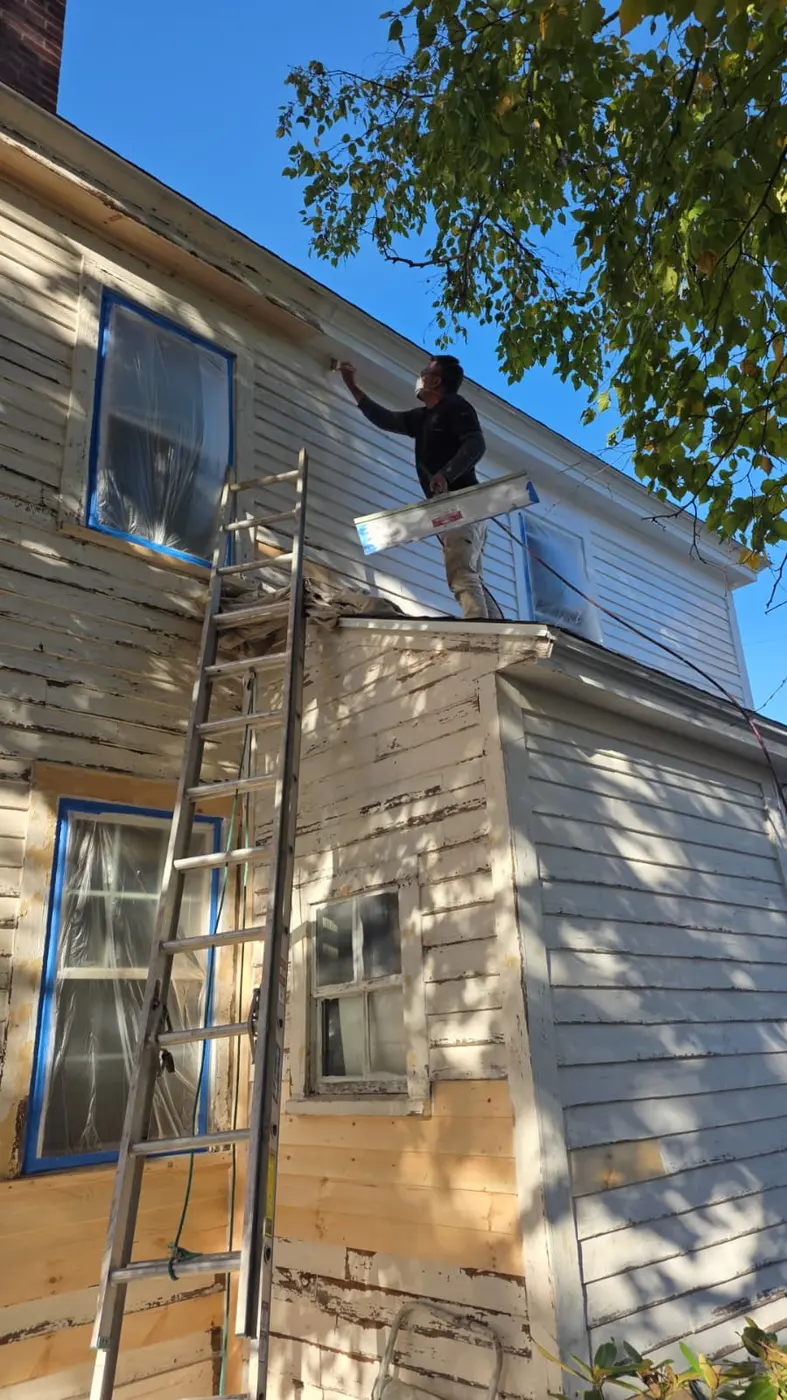 Painter on a ladder scraping and painting the siding of a Massachusetts home